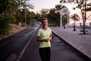 Young woman in sportswear runs along the path at dawn. Morning routine, meditation, feeling of freedom. Girl is wearing black leggings and a yellow T-shirt. Beautiful red sky. Concentrated motivation