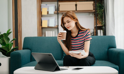 Female students note from the books at the Asian girl library sitting at sofa using laptop computer and tablet to search an online informations.