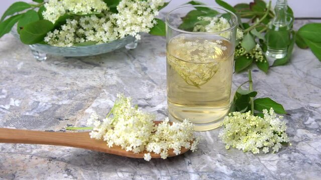 Homemade elderflower drink with sugar and lemon in a glass, light background