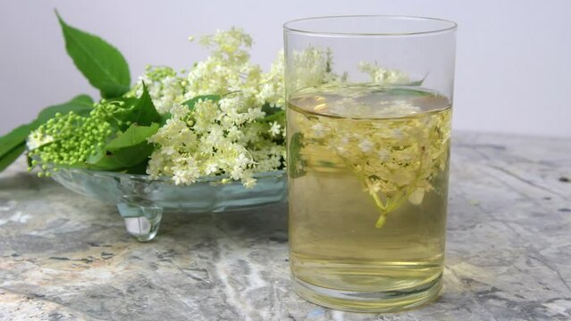 Homemade elderflower drink with sugar and lemon in a glass, light background