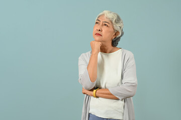 Thoughtful senior woman thinking and looking up expressing doubt and wonder isolated blue background