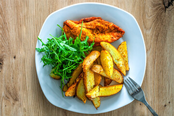 Plate with baked potatoes, meat, arugula leaves on dining table. Gourmet baking dinner, top view