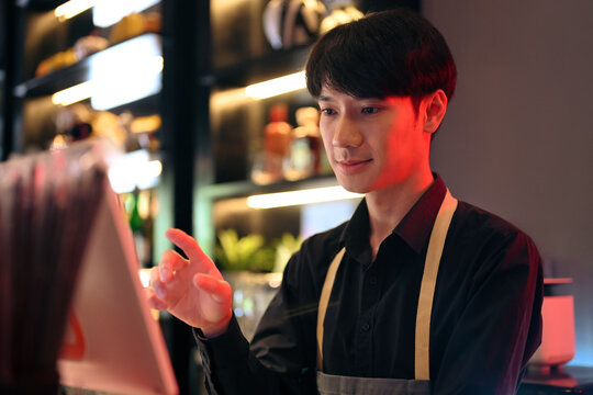 Handsome male waiter touching display of electronic cash register, entering customer order at bar or coffee shop - Powered by Adobe