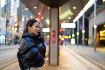 Asian woman using mobile phone during waiting for train at railway station. Attractive girl enjoy urban outdoor lifestyle travel city street with using wireless technology device on holiday vacation.