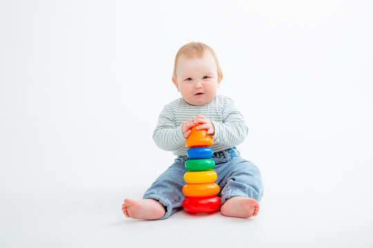 charming baby in a T-shirt and jeans is playing with toy pyramid, a postcard, a banner, a place for text. High quality photo