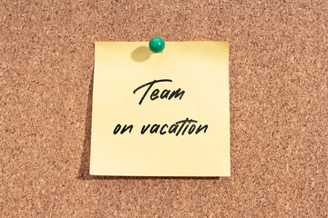 Yellow sticky note with message Team on Vacation on cork board