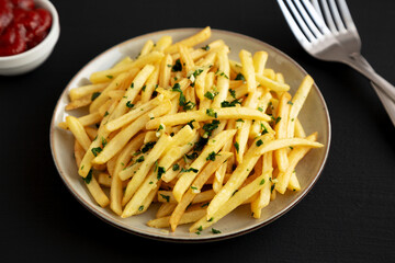 Garlic French Fries with Parsley on a Plate on a black background, side view.