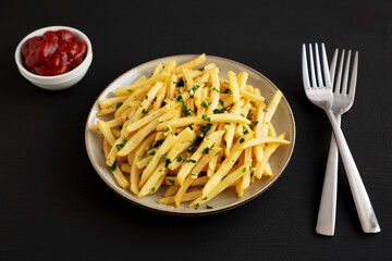 Garlic French Fries with Parsley on a Plate on a black background, side view.