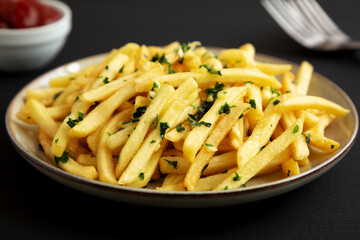 Garlic French Fries with Parsley on a Plate on a black background, side view. Close-up.
