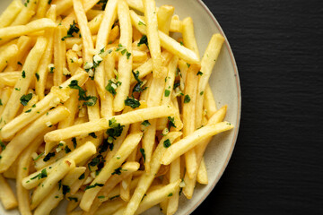 Garlic French Fries with Parsley on a Plate on a black background, top view. Overhead, from above, flat lay.