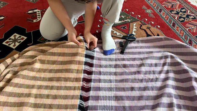 A woman is cutting the handmade textile cloth to make curtain with yellow purple pattern inside the house in the room sewing tailoring concept in rural life in the village in Iran Khorasan art weaving