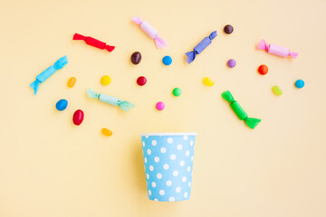 Different kinds of colorful candy out of a blue paper cup with white dot on yellow background, Various candies