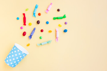 Different kinds of colorful candy out of a blue paper cup with white dot on yellow background, Various candies