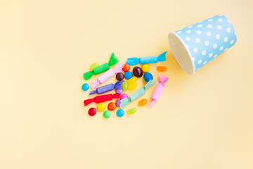 Different kinds of colorful candy out of a blue paper cup with white dot on yellow background, Various candies