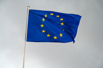 EU flag waving in the wind against dark cloudy sky. Flag of European Union flying on a pole. 