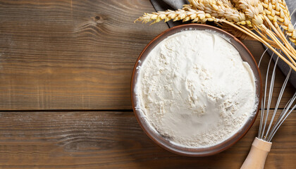 Flour in ceramic bowl with a handful with ears of wheat and beater on the wooden table closeup. Top...