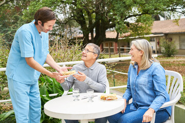 Caregiver with senior people having meal in garden of nursing home