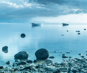 Boats in calm waters with rocks and overcast weather