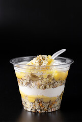 Takeway cake in a glass with poppy seed cake, curd cream and lemon curd on black background, Vertical image