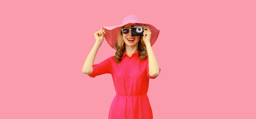 Summer portrait of happy smiling young woman photographer with film camera wearing straw hat, pink dress, sunglasses on background
