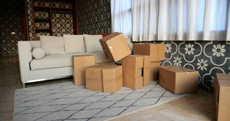 Scattered cardboard boxes in living room create messy pile. In slow motion, empty box flies in and joins jumble of boxes. Scene portrays remnants of child's play, with hint of required cleaning