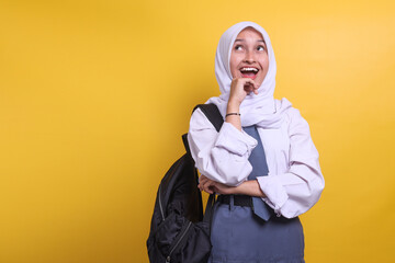 Happy Indonesian high school female muslim student in white and grey uniform looking up at copy space