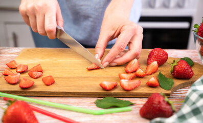 Women's hands cutting strawberry for lemonade on the table in the kitchen. Close-up. Selective focus.