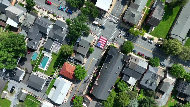 Flying above a town as an Independence Day parade moves up the main street. Top down aerial orbit.