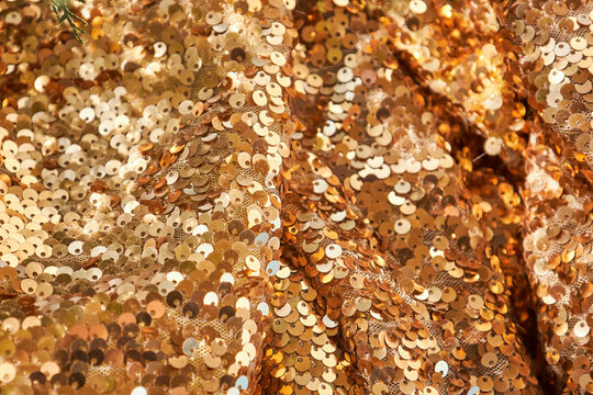 Waves of brightly shiny fabric with large gold sequins. Festive rich textiles glitter mesh for dresses. High quality photo, texture background.