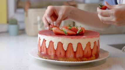 Close-up of a woman's hands decorate a fresh strawberry cake
