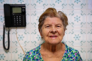 portrait of hispanic mature adult woman smiling in a retro-style kitchen with a phone