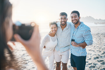 Happy, photo and friends at the beach with a photographer for summer memory, holiday or bonding. Smile, camera and a woman taking a picture of a group of people at the ocean during a vacation - obrazy, fototapety, plakaty