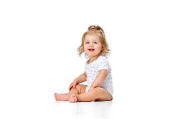 Beautiful, happy, smiling child. Little baby girl, toddler sitting on floor with joy and fun against white studio background