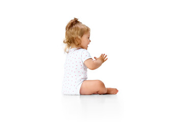 Positive, happy, carefree little girl child sitting on floor and clapping hands in joy and fun against white studio background