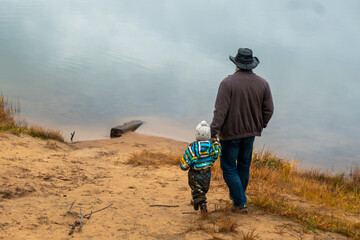 A happy family of two is standing on a cloudy autumn day on the bank of the lake