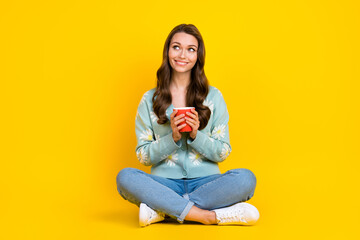 Obraz na płótnie Canvas Full body photo of young attractive lady sitting relaxed hold cup of aromatic coffee look empty enjoy mornings isolated on yellow color background