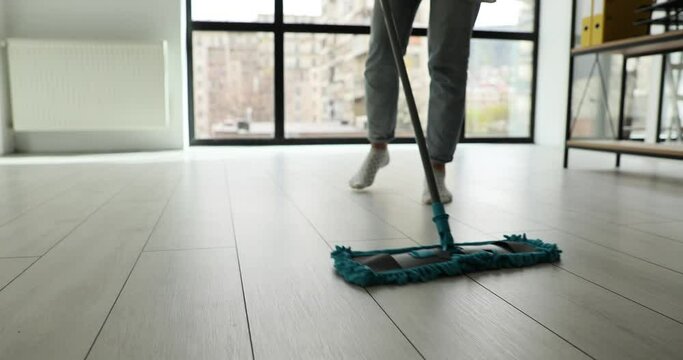 Housewife cleans floor with wet mop in living room or in office. Woman removes dirt from laminate flooring surface at home