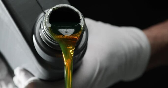 Motor oil is pouring from a canister in hand on black background. Oils and lubricants for car