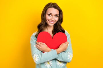 Photo of sweet adorable woman wear turquoise cardigan smiling embracing red heart isolated yellow color background