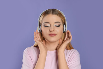 Beautiful woman in headphones enjoying music on violet background