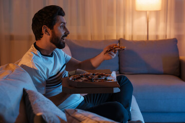 Man eating pizza while watching TV on sofa at night. Bad habit