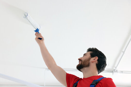 Handyman painting ceiling with roller in room, low angle view