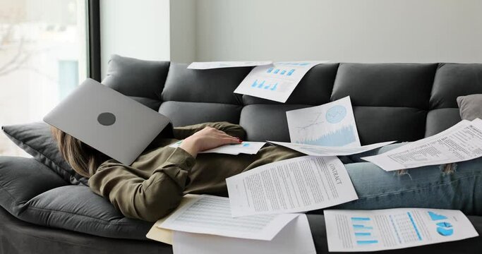 Tired female student sleeps at home on couch with documents and does research and prepares and writes dissertation. Hard work freelancer and overtime work