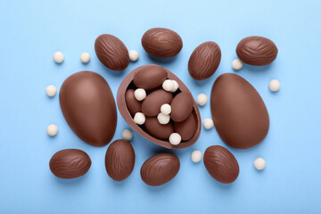 Delicious chocolate eggs and candies on light blue background, flat lay