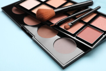Colorful contouring palettes with brushes on light blue background, closeup. Professional cosmetic...