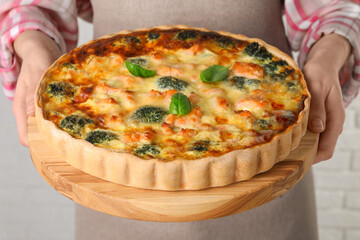 Woman holding delicious homemade quiche with salmon and broccoli on light background, closeup