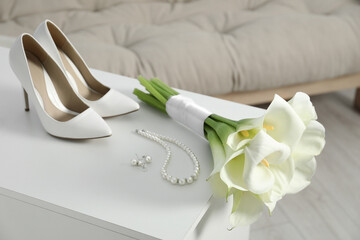 Beautiful calla lily flowers tied with ribbon, shoes and jewelry on white chest of drawers indoors