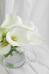 Beautiful calla lily flowers in glass vase on white cloth