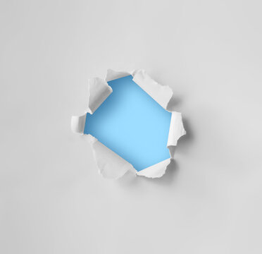 Torn hole in plain white paper with a blue background. Concept for advertising.