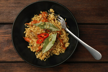 Delicious pilaf, bay leaves and fork on wooden table, top view